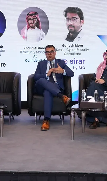 Panel discussion on a conference stage with four speakers seated against a projection screen in Riyadh